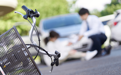 a knocked-down bicycle in the foreground of a bicycle accident victim being helped by the driver who hit her.