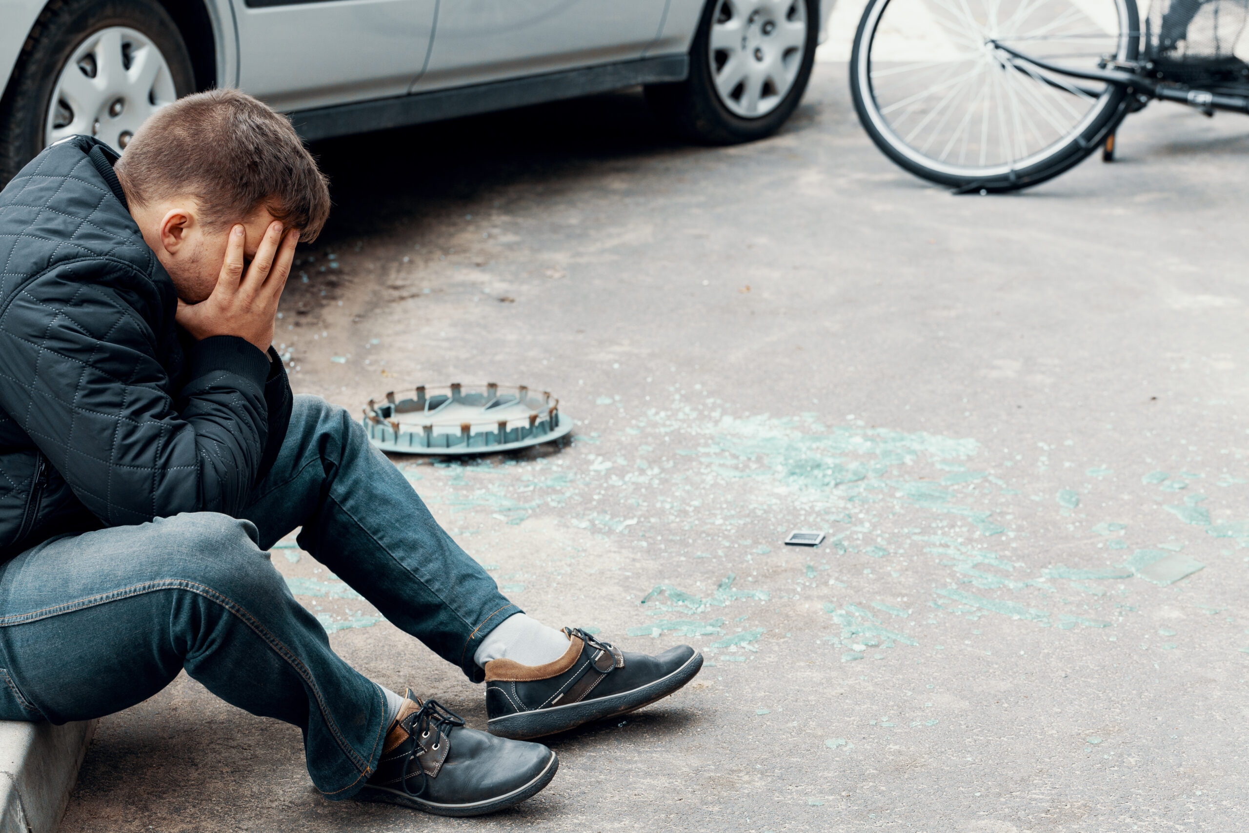 Man sitting on street after accident with a vehicle and a bicycle