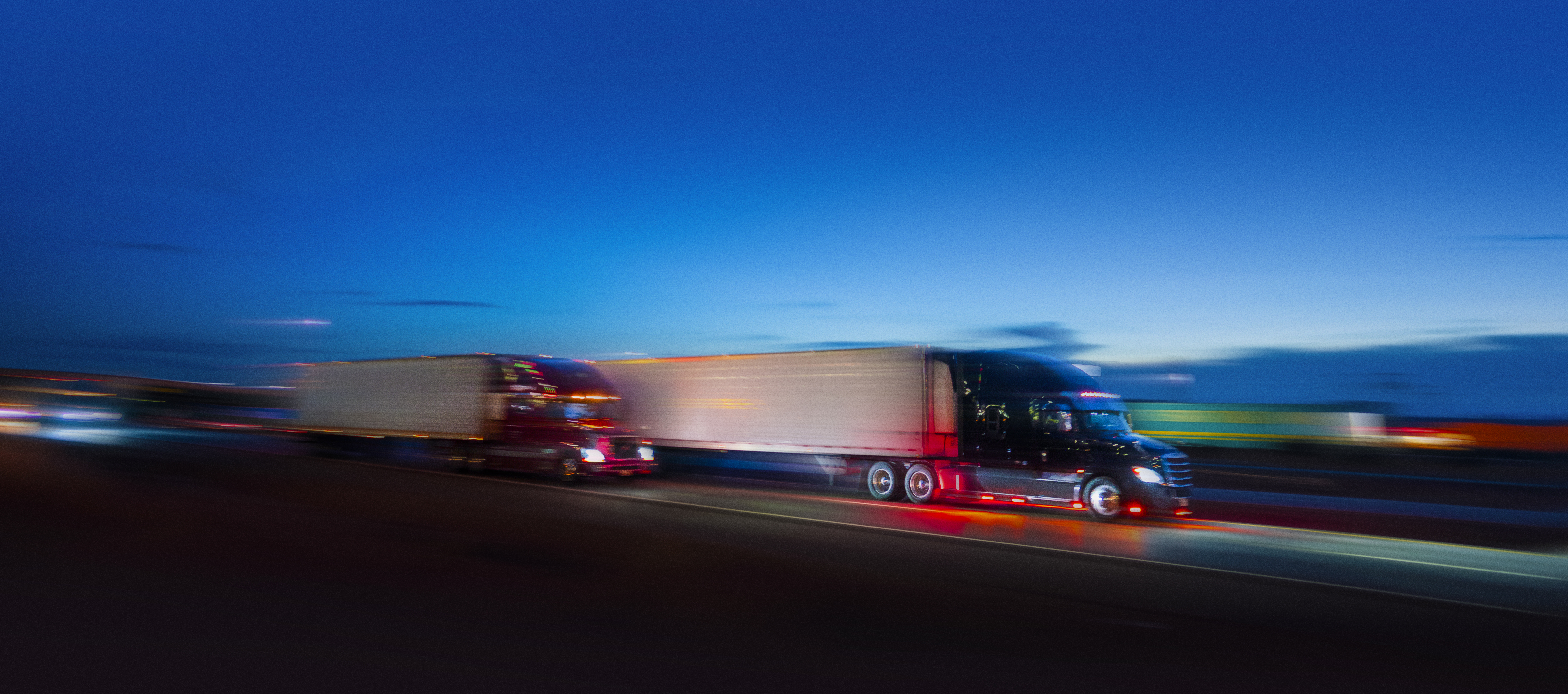 two large semi-trucks are blurred as they appear to be traveling at a high rate of speed on a highway.