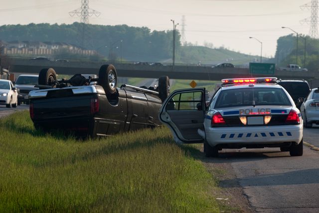 A large, black SUV is rolled over in the median of the highway. Police are on the scene.