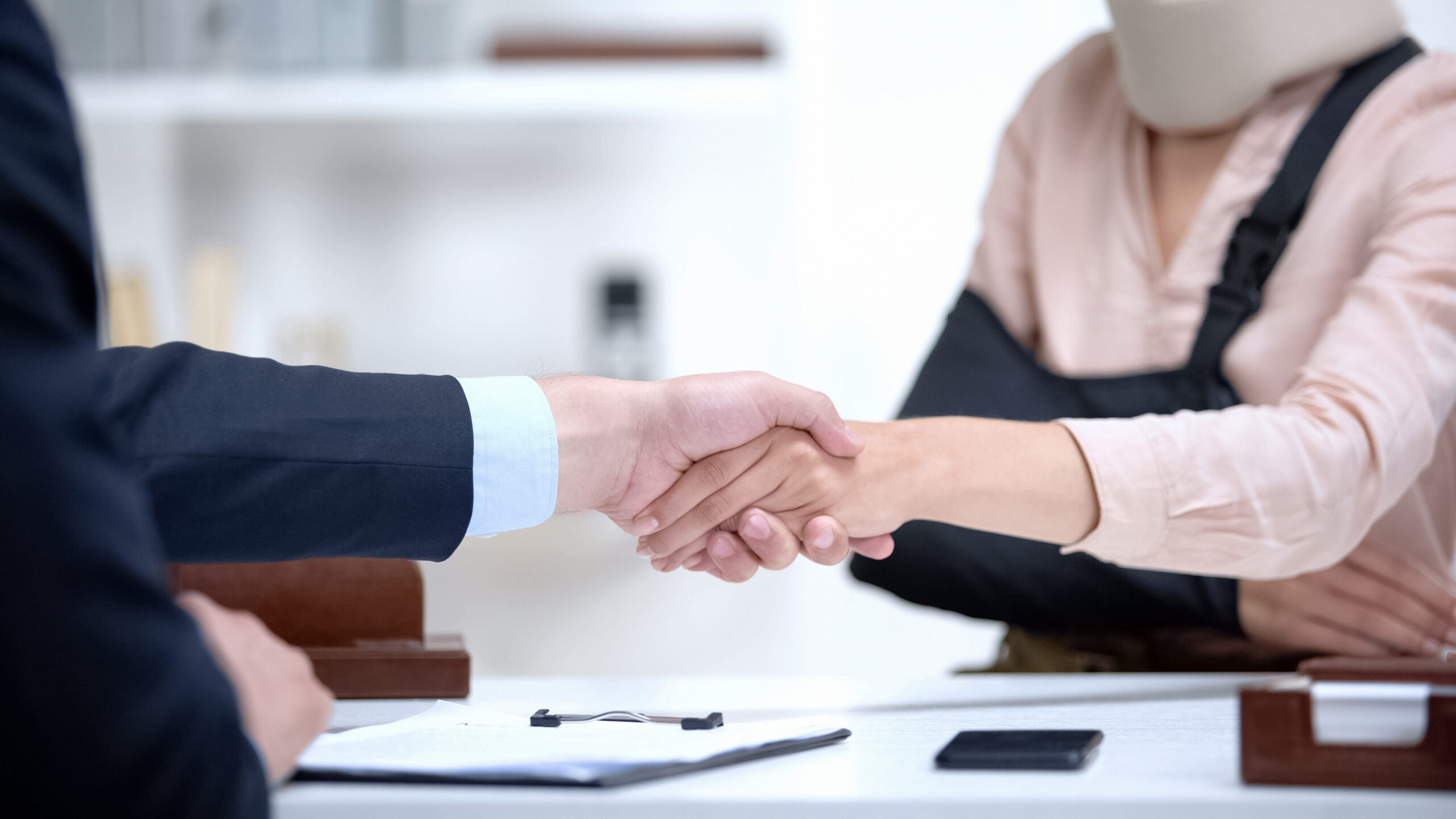 A woman with her right arm in a sling shakes hands with her personal injury lawyer after a consultation.
