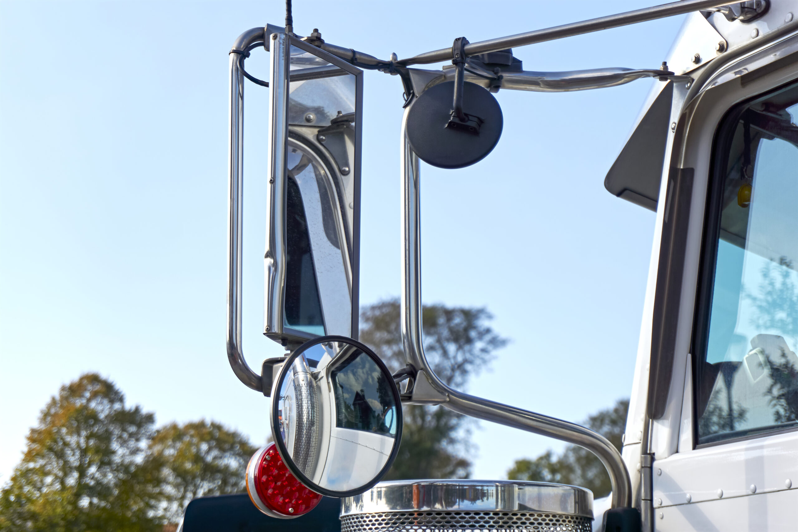 Closeup of mirrors on a cargo truck. Rear view mirror and blind spot mirror on the outside of a white freight truck against a blue sky. 