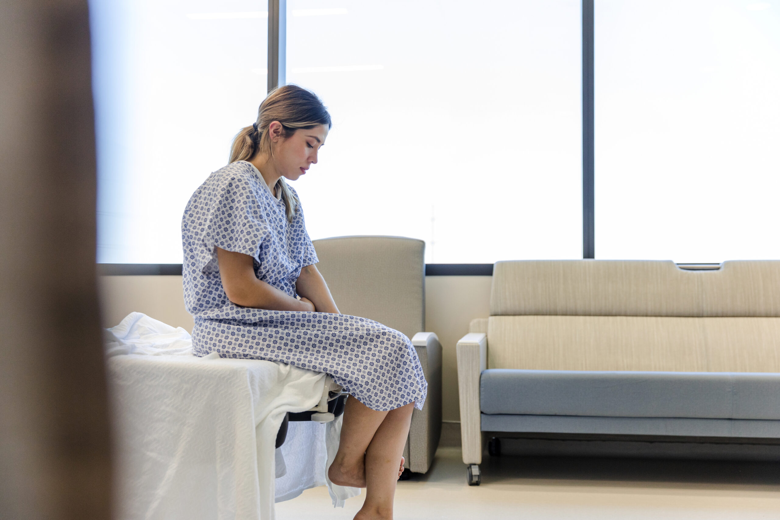 A woman sits on the edge on a hospital bed awaiting an examination after experiencing a personal injury