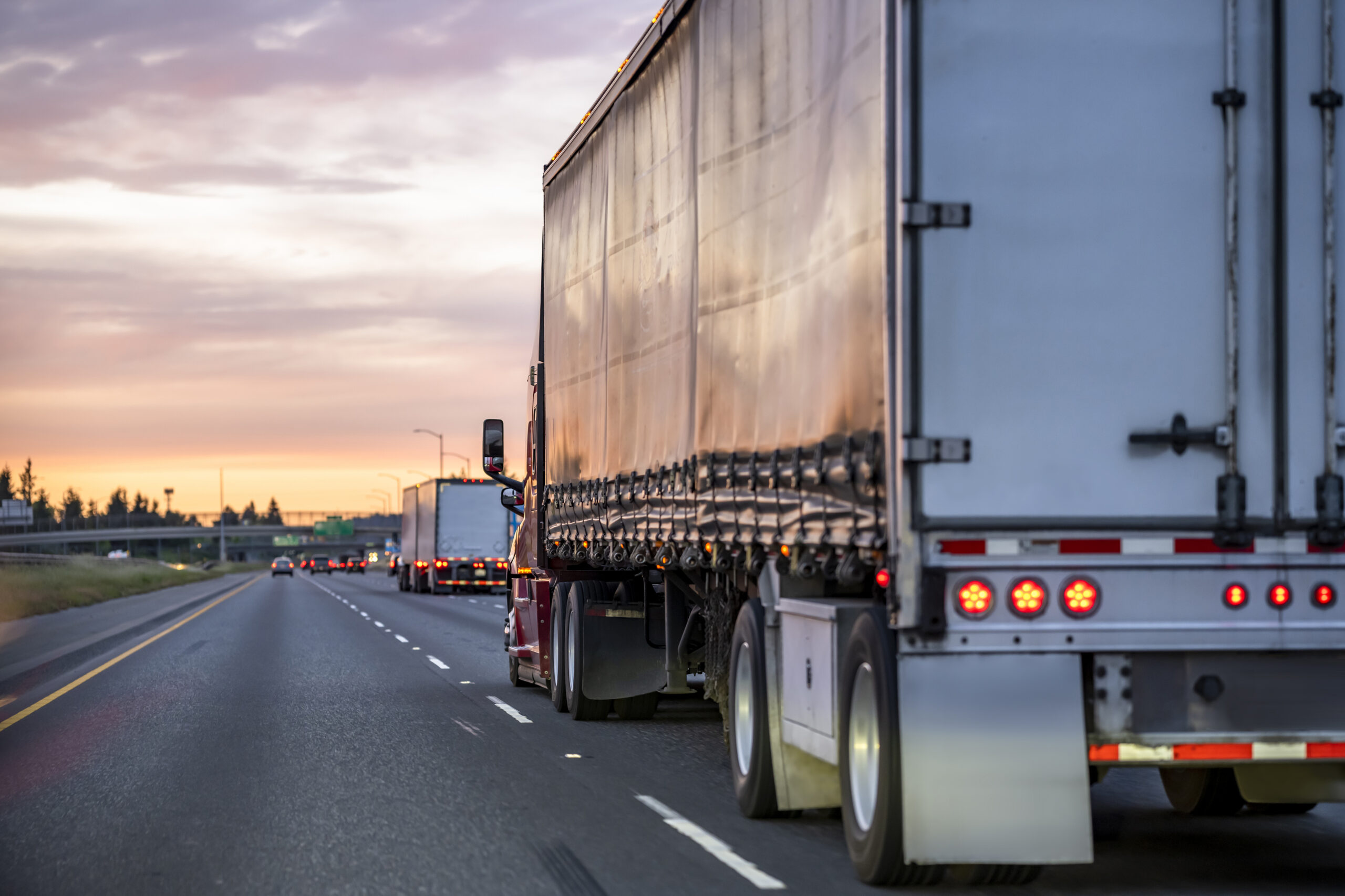 A car approaching the blind spot of a semi-truck traveling down a three-lane highway.